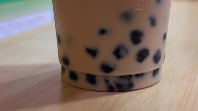 Macro close up of black boba pearls swirling and mixing inside a creamy bubble milk tea drink, highlighting the chewy tapioca balls and popular Asian beverage.