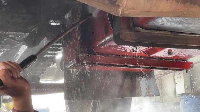 Truck underbody washing captures a pressure spray reaching the frame and exhaust components, with water droplets and runoff visible as the vehicle receives full cleaning during service here.