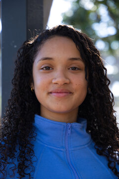 African American teenage female smiling wearing blue fleece, gold hoop earrings at park near pillar