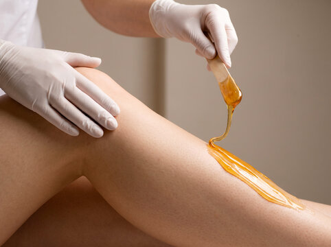 Beautician applying sugar paste to woman's leg during sugaring hair removal procedure