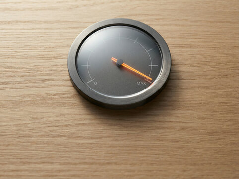 Circular gauge with an orange needle centred on a light wooden tabletop
