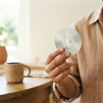 Person holding out a compact disc in a warm kitchen with a bright window