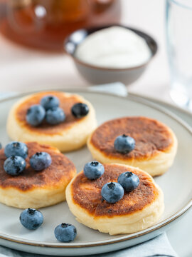 Delicious homemade curd pancakes served with blueberries on a plate. Healthy morning breakfast with sour cream, sweet recipe idea. Bright clean background with copy space for banner design