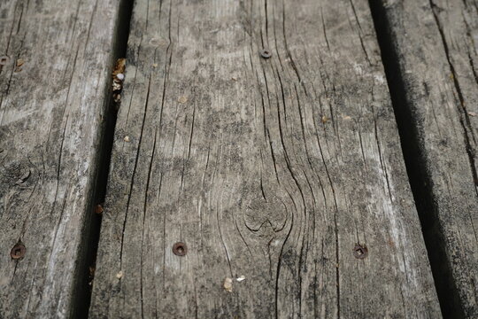 Close-up of weathered grey wooden planks with prominent grain cracks and rusty nails showcasing a rustic aged texture and natural deterioration