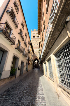 Narrow street leading to San Martin Mudejar tower in Teruel Spain. Historic cobblestone alleyway, traditional buildings and brick tower. High quality photo