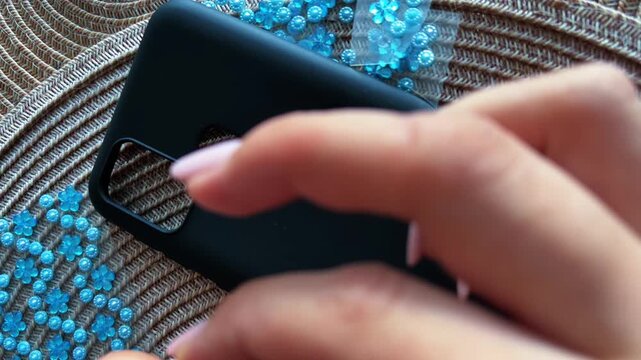 Woman's hands customizing a black smartphone case with adhesive blue rhinestones, creating a unique handmade design for a mobile phone accessory with diy jeweled decoration