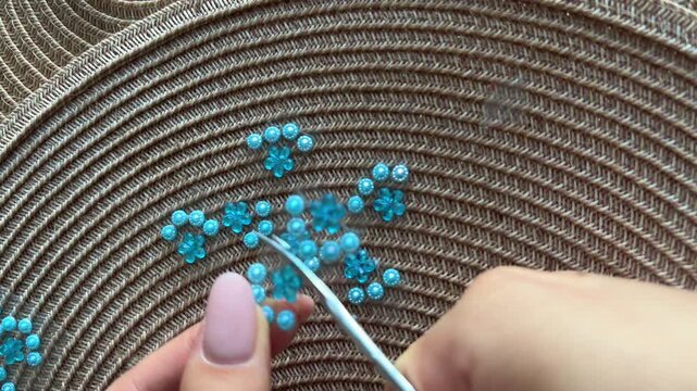 Artisan's hands stringing intricate blue flower beads and pearls with a crochet hook for creating handmade jewelry, showcasing a traditional beading craft technique