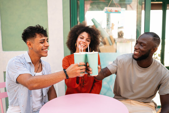 Three happy friends toasting refreshing summer drinks at a vibrant outdoor cafe, celebrating the joy