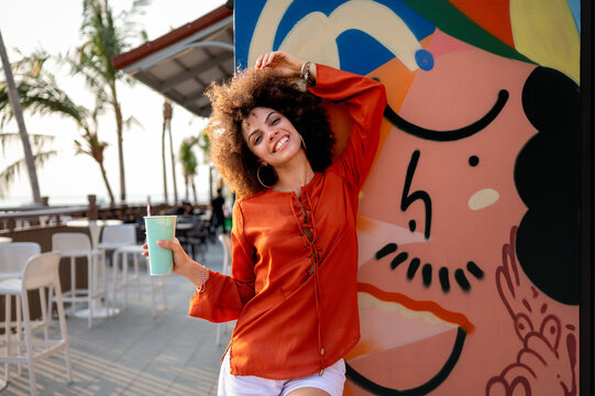 Architectural elements meet urban art as a young happy woman stands against a textured wall