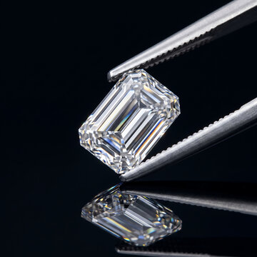 Emerald cut diamond held by metal tweezers against a black background
