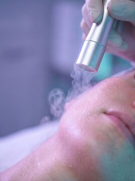 Therapist holds the cryotherapy nozzle to woman's cheek, with light frosty steam visible in the frame. Cryotherapy treatment, aesthetic cosmetology concept. Close-up shot for commercial poster