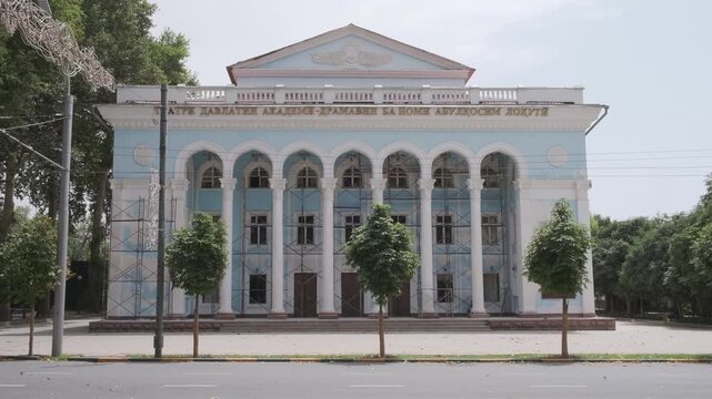 Grand Soviet-era theater with imposing columns and passing cars on a city road