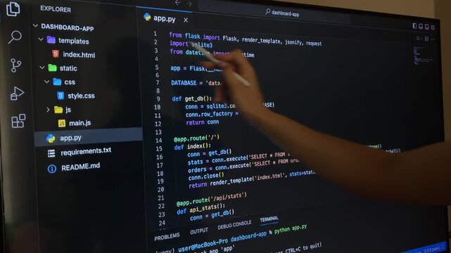 Programmer pointing at computer monitor displaying python code and explaining software development process, focusing on code structure, functions, and file organization