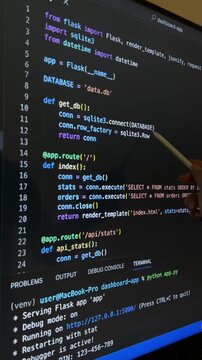 Teacher explaining python code for a web application using flask and sqlite, pointing to functions and sql queries for educational purposes on a computer screen