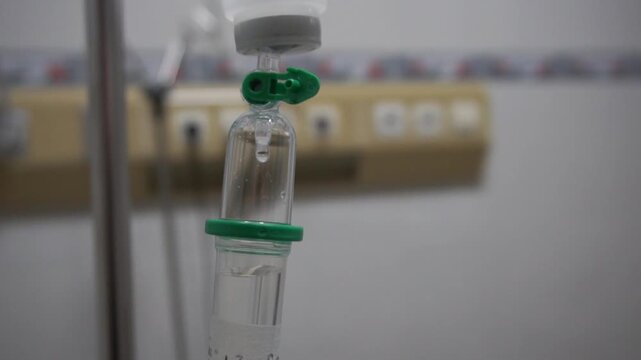 Close up intravenous drip chamber with saline solution drop in hospital room, medical iv fluid therapy equipment concept for health care and treatment.