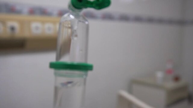 Close up intravenous drip chamber with saline solution drop in hospital room, medical iv fluid therapy equipment concept for health care and treatment.