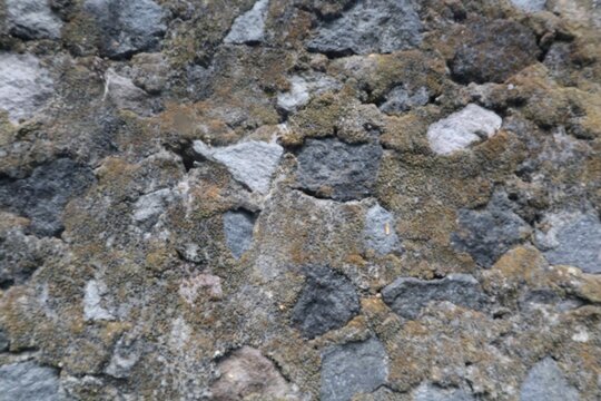 Close-up of an old fence wall built from rough basalt stones, showing weathered texture, natural rock colors, and rustic masonry details.