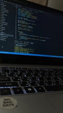 Close up of laptop screen displaying programming code with an illuminated keyboard, focusing on software development, web app creation, and cybersecurity concepts