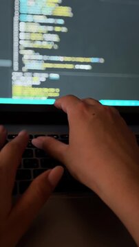 Female programmer's hands typing code on a laptop keyboard in a dark office, with the monitor reflecting programming language and data, illustrating software development