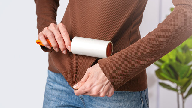 Close up woman cleaning dark clothing with adhesive sticky roller in home interior. Concept minimizing lint, pet hair and maintaining clean appearance through practical garment maintenance routine