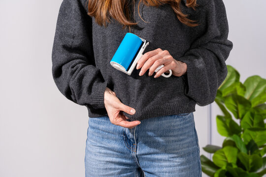 Woman cleaning dark sweater with reusable ecofriendly sticky roller to remove visible lint and pet hair in light home interior. Concept of minimizing lint on black clothing and everyday garment upkeep