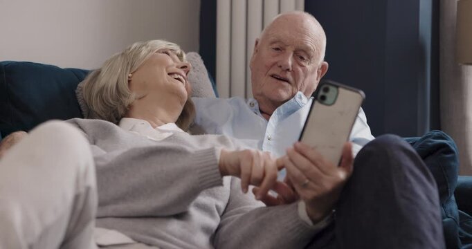 Speaking, phone and happy old couple laugh, talking and reading funny online news article, blog post or social media. Love hug, bond or relax elderly man, woman or home people laughing at meme joke