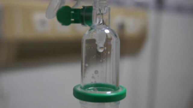 Close up intravenous drip chamber with saline solution drop in hospital room, medical iv fluid therapy equipment concept for health care and treatment.