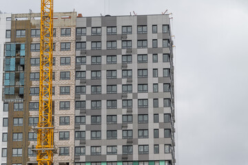Construction progress on a modern high-rise building with a yellow crane against an overcast sky in the cityscape © beholdereye