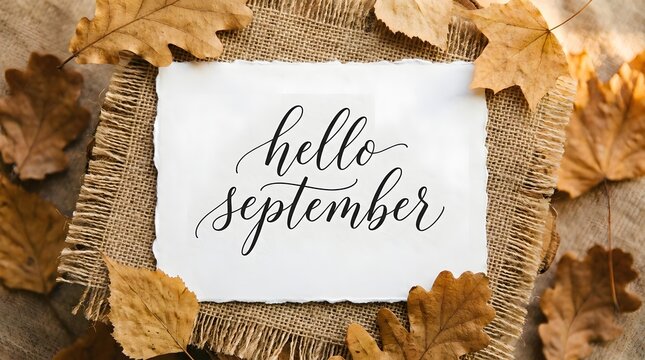 Hello september calligraphy on a piece of paper placed on burlap fabric surrounded by dry autumn oak leaves