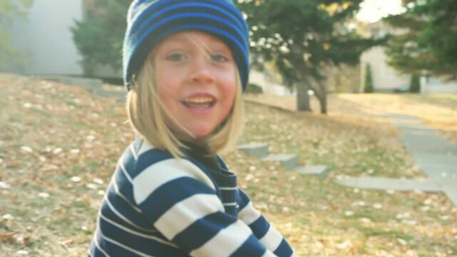 Boy in a striped beanie smiling while holding a pink tricycle in an autumn park