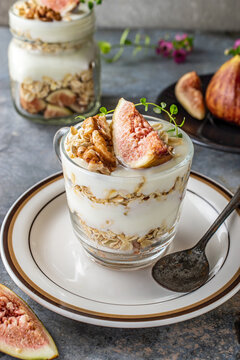 Healthy Greek yogurt parfait layered with wholesome rolled oats, fresh figs, walnuts, and natural honey served in glass jars. Delicious organic clean eating breakfast for wellness lifestyle.