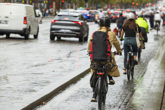 Eco-friendly urban transportation and cyclists riding on a wet Parisian bicycle path next to traffic during a rainy day commute in France