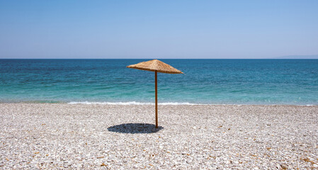 Lone straw parasol casting shadow on white pebbles at Giosonas Beach, Chios, Greece © Rawf8
