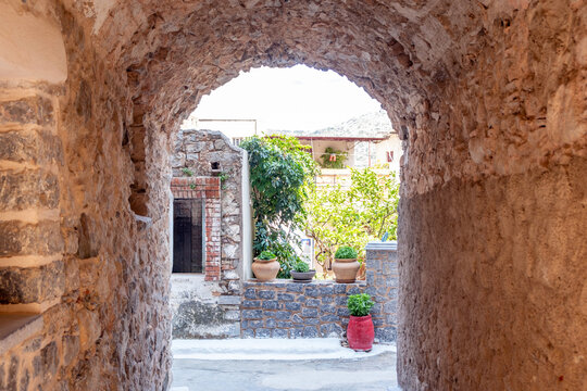 Stone arch framing narrow street with potted plants in Olympoi, Chios, Greece