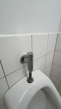 Hand pressing the chrome flush button of a urinal in a white tiled public restroom, vertical POV clip on shared surfaces, hand hygiene and germ contact in daily life
