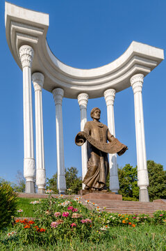 View of the bronze statue of astronomer and mathematician Ahmad al-Farghani standing beneath a white colonnade with colorful flowers in the foreground in Fergana, Fergana Region, Uzbekistan.