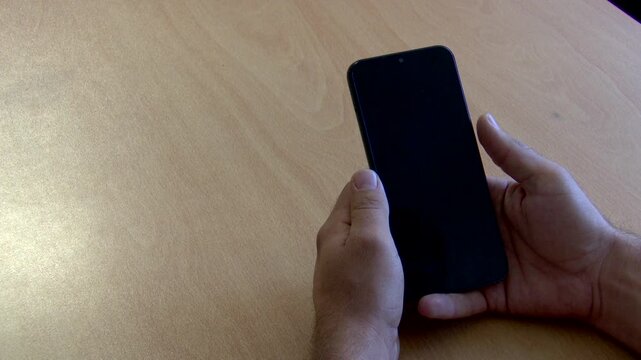 High-resolution 4K close-up video of a hand unlocking and scrolling on a sleek black Android smartphone resting on a wooden table, revealing a clean, solid white screen. Ideal for mobile app mockups, 