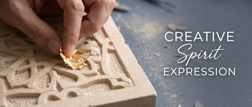 Craftsman hands applying gold leaf onto carved stone relief pattern in artisan workshop, demonstrating intricate gilded restoration art, traditional craft precision, and luxury ornament design heritag