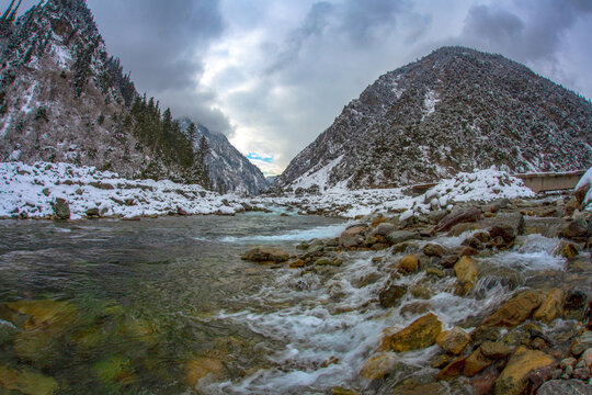 View of the Swat River flowing through snow-covered mountains in the winter season with rocky banks and a cloudy sky in Kalam, Khyber Pakhtunkhwa, Pakistan.
