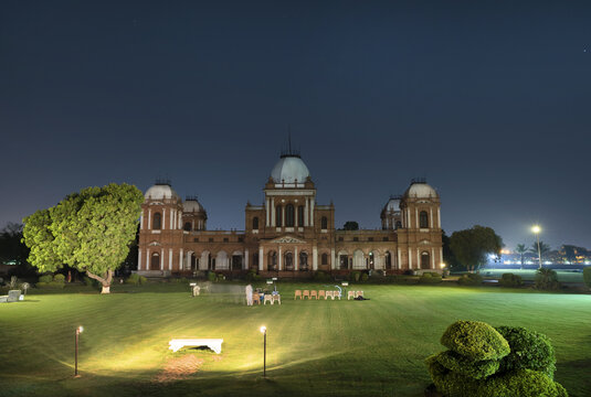 View of Noor Mahal illuminated at night with a manicured lawn and trees in Bahawalpur, Punjab, Pakistan.