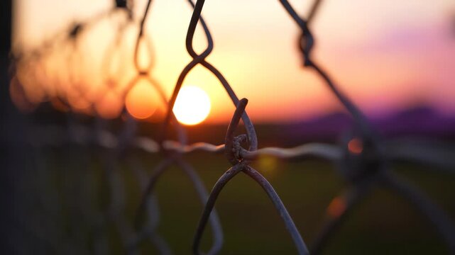 Macro close up of intertwined metal wire fence links with a soft bokeh sunset background as the camera slowly glides along the mesh