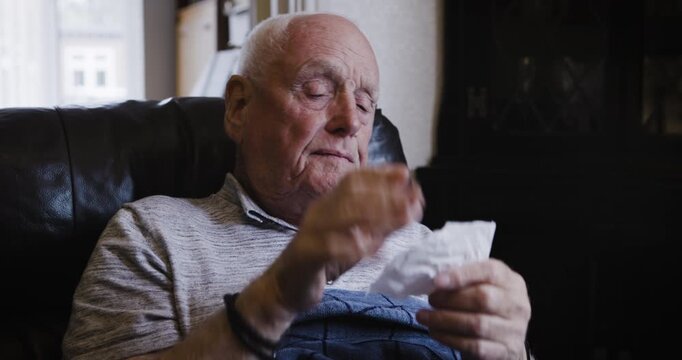 Sick senior man, cough and cleaning nose and tissue, tired or suffering from flu virus, cold or covid in home. Elderly male with bad allergy or coronavirus sneezing with a sinus or allergies on sofa
