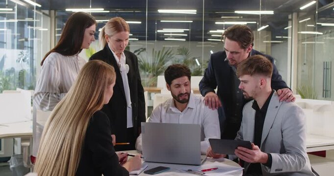 Young motivated team busy planning, discussing creative startup ideas, employees group looking at laptop screen to share successful result, modern workers brainstorming in modern glass office zone