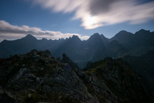 View of Mlynar peak in the High Tatras mountains under a moonlit sky with moving clouds over the rocky terrain in Tatranska Javorina, Presovsky kraj, Slovakia.