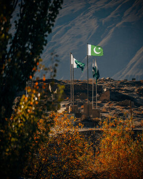 View of the Pakistani flags waving in the Hunza Valley, framed by autumn foliage and rugged mountain peaks in the background in Hunza Nagar, Gilgit, Pakistan.