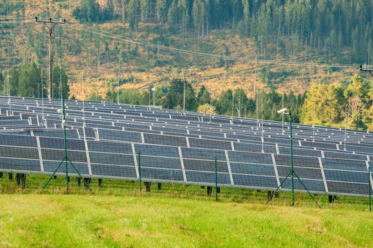 View of solar panels in a grassy field with a forest backdrop and security cameras at the Jakubovany solar farm in Liptov, Presov Region, Slovakia.
