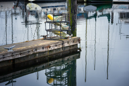 View of a crab trap resting on a wooden pier with calm water reflections in Charleston harbor, Charleston, Oregon, United States.