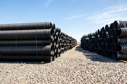 View of stacked black corrugated plastic pipes arranged in rows on a gravel surface under a clear blue sky in Eugene, Oregon, United States.