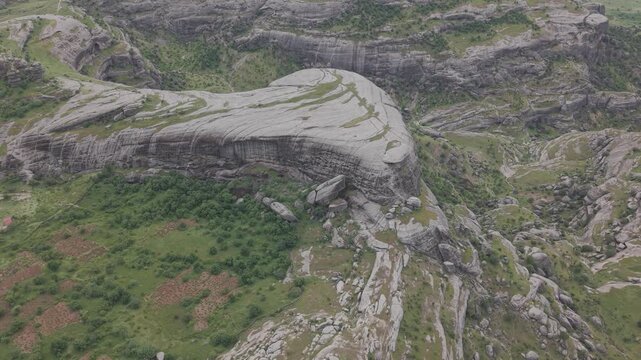 Smooth 4K 30fps bird's eye flight over a massive oval rock with a distinctive foot like shape. Shot in a flat color profile, ready for color grading and LUT application.