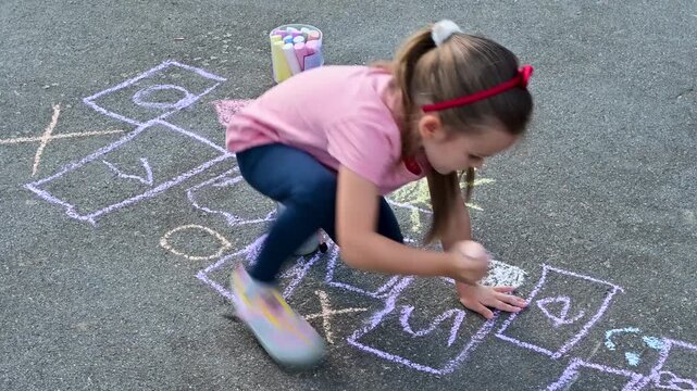 Preschool toddler girl drawing hopscotch grid with chalk on asphalt pavement. Perfect footage for childhood activities, education and summer lifestyle content. 4K slow motion footage